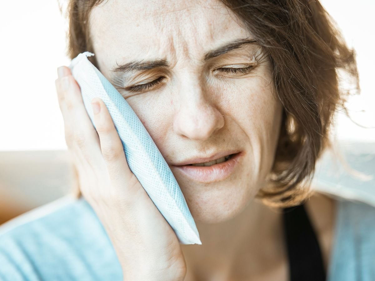 Woman holding a cold compress against her cheek while experiencing severe tooth pain and dental discomfort at home.